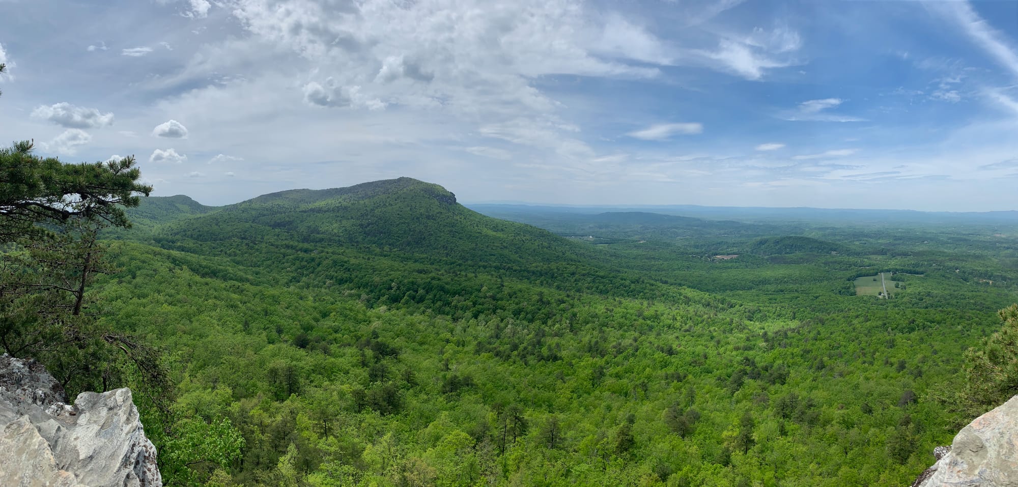 Wide shot photo of a valley of trees and mountains with blue skies and clouds. 